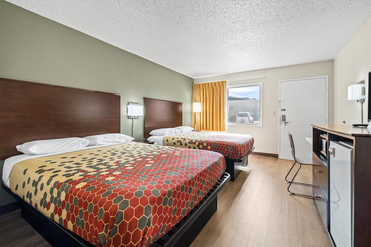 A hotel room with two beds, a desk, and a window with a view.