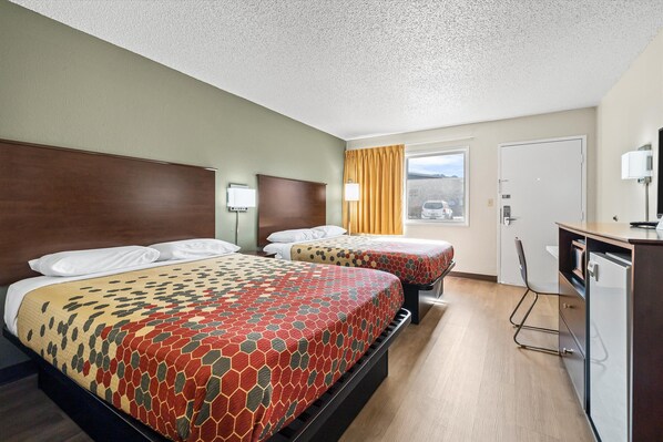 A hotel room with two beds, a desk, and a window with a view.