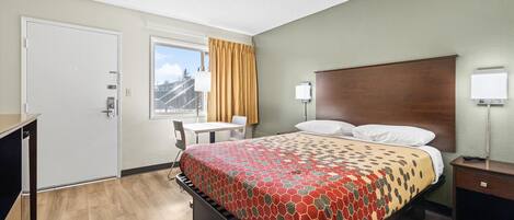 A hotel room with a bed, a desk, a chair, a window with curtains, and a nightstand.