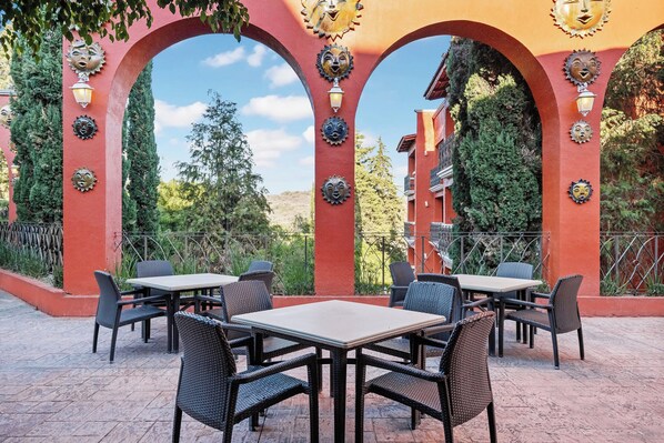 An outdoor patio area with tables and chairs, surrounded by red arches with decorative sun motifs. - Fiesta Americana Hacienda Ixtapan de La Sal (Ixtapan de la Sal)