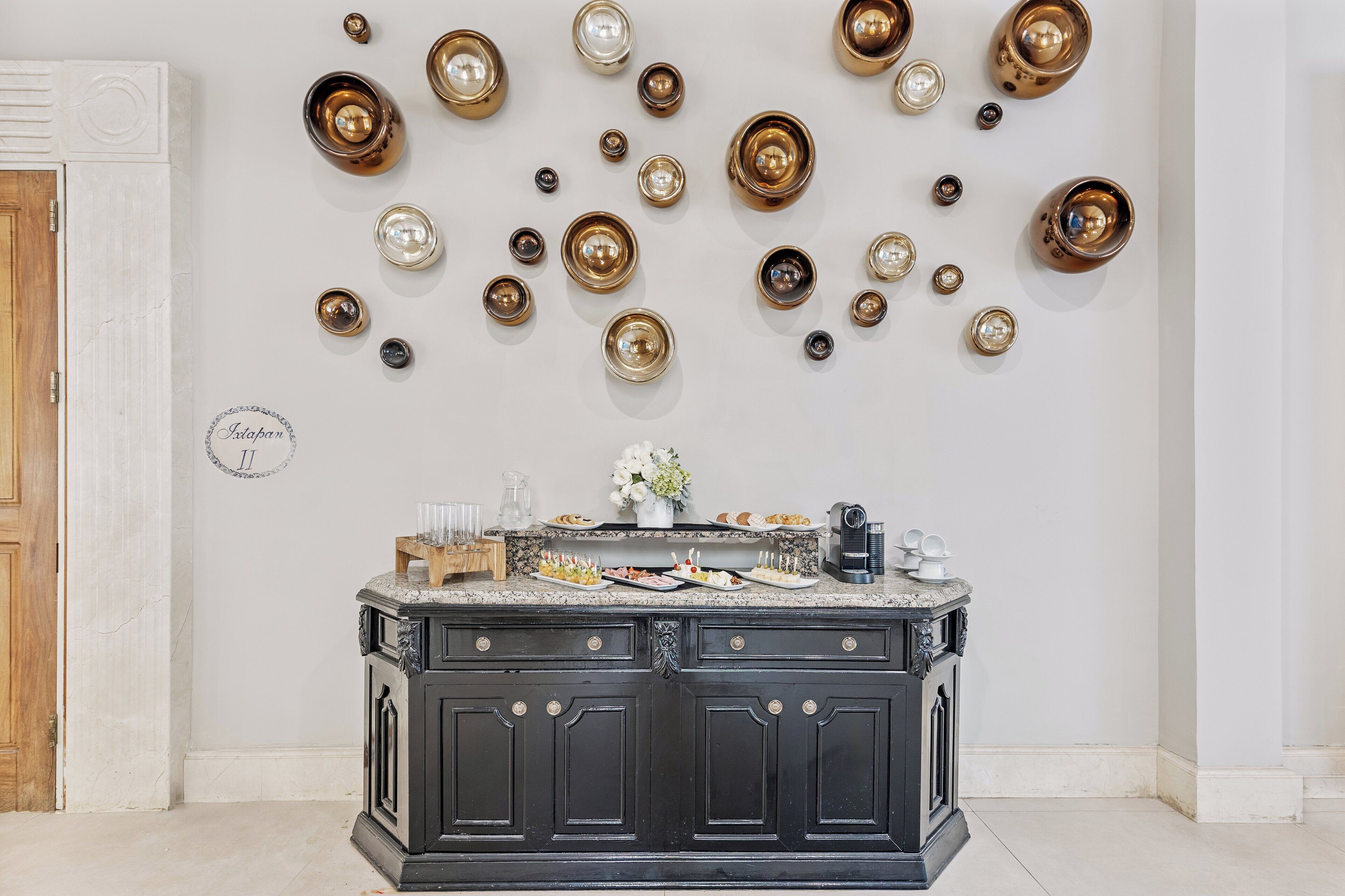 A kitchen with a marble countertop, black cabinets, and a wall decorated with various metal bowls and plates.