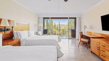 Habitación de hotel con dos camas, un escritorio, una silla, un televisor y un balcón con vistas a árboles.