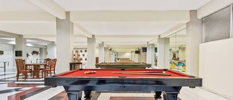 A pool table in a spacious indoor area with a checkered floor, wooden chairs, and a dining table in the background.