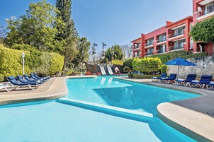 Una piscina con sillones de descanso, un edificio rojo y un jardín bien cuidado.