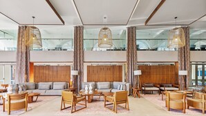Un hall d’entrée spacieux avec un plafond haut, de grandes fenêtres et un aménagement intérieur moderne comprenant un canapé, des fauteuils et des tables.