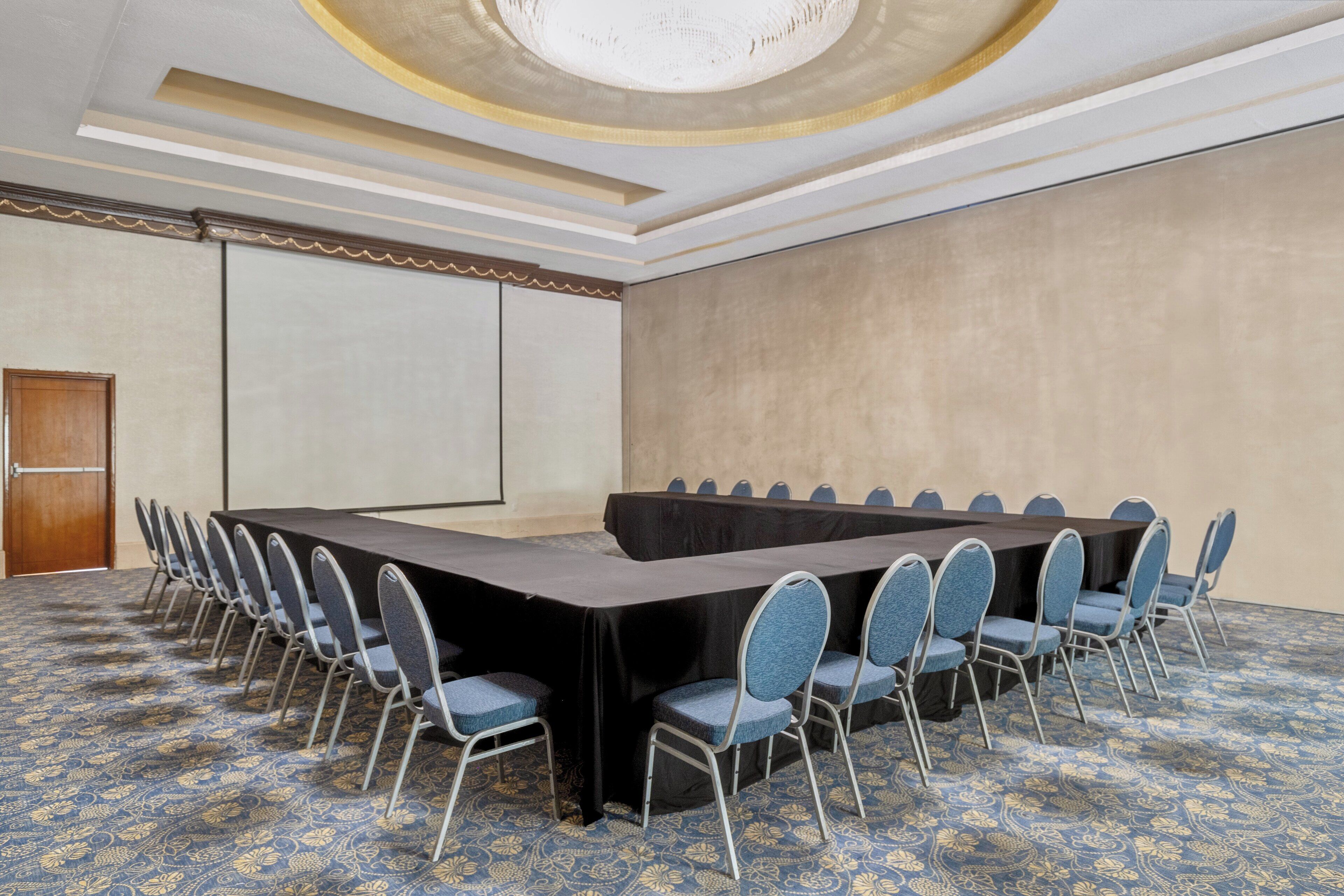 A conference room with a long table and chairs, a carpeted floor, and a plain wall.