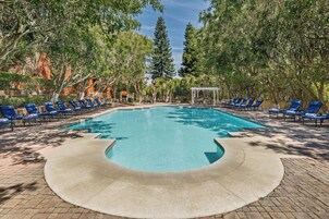 Una piscina con sillas reclinables azules y un pabellón, rodeado de árboles.