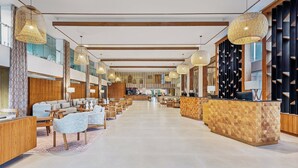 Eine geräumige Lobby mit Empfangstresen, Sitzgelegenheiten und hohen Decken mit hängenden Lampen.
