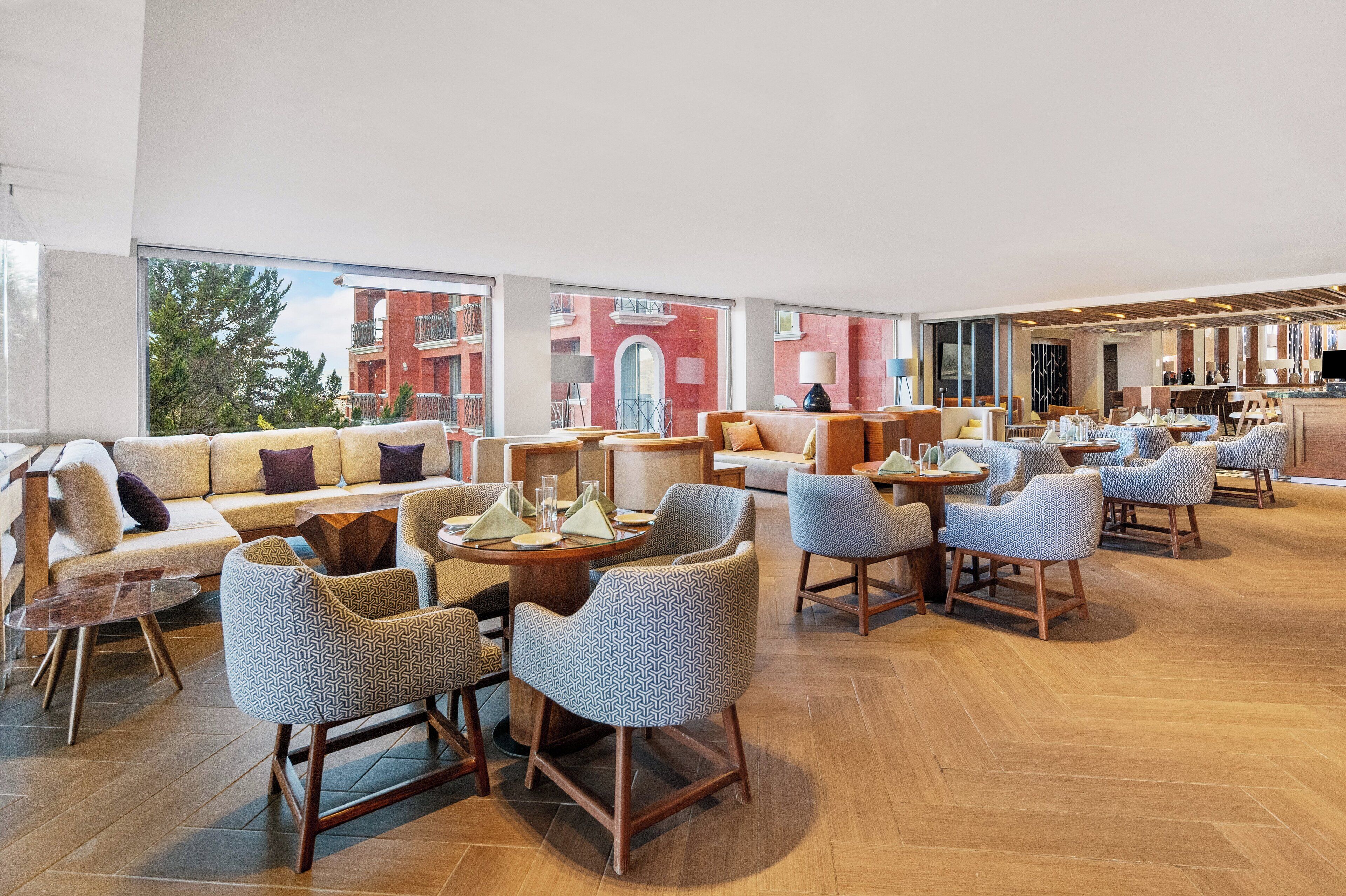 Un vaste espace salon doté de nombreux sièges, notamment des canapés et des fauteuils, disposés autour d’une table basse centrale. De grandes fenêtres offrent une vue sur l’extérieur du bâtiment.