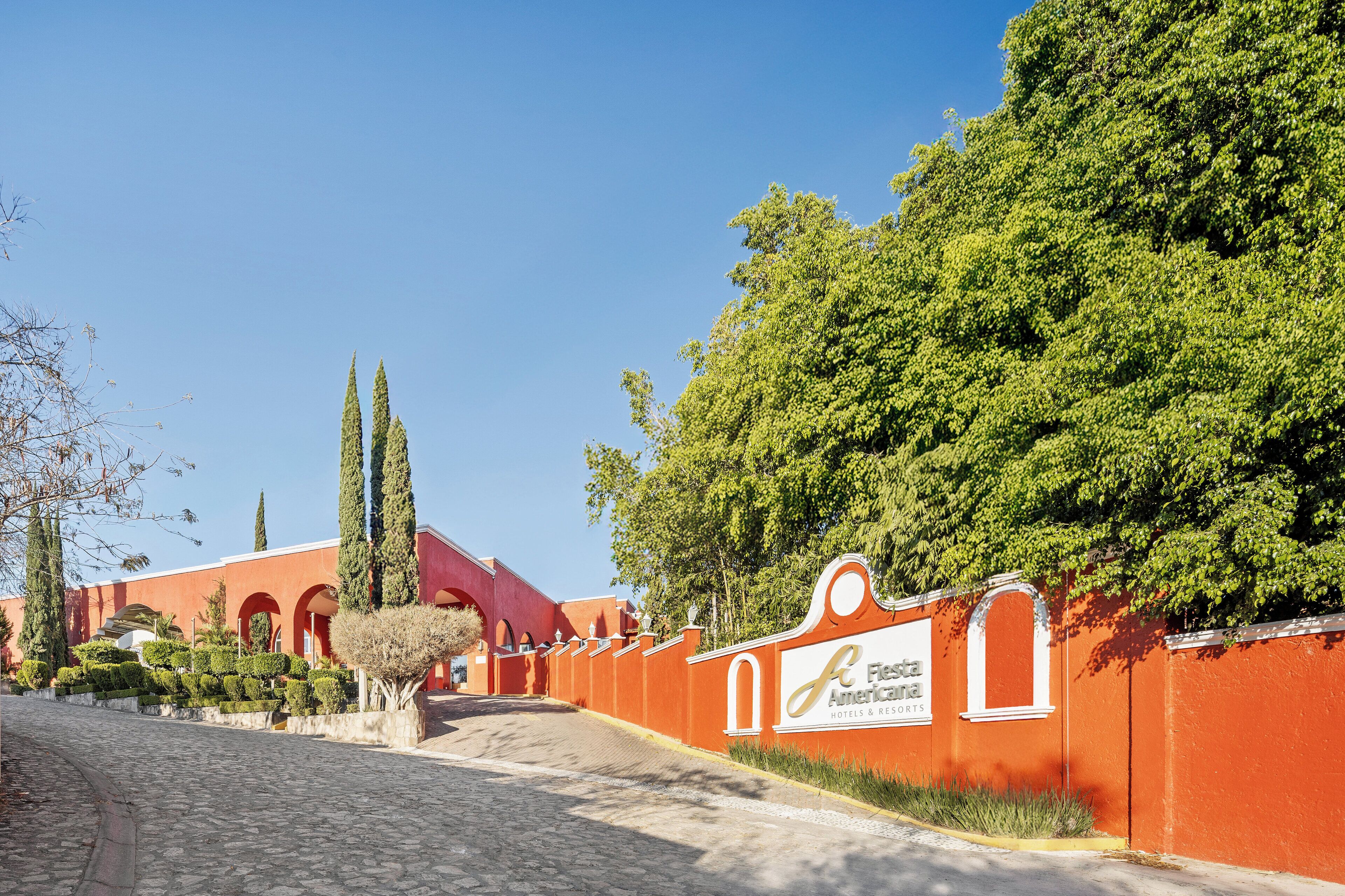 A pathway leading to a building with a red facade and a sign for 'Festa Americana Hotels & Resorts'.