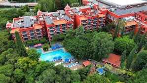 Un grand hôtel rouge, à plusieurs étages, doté d’une piscine entourée d’une végétation luxuriante.
