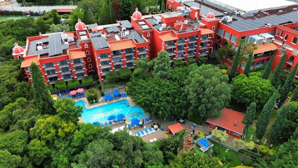 Ein rotes, mehrstöckiges Hotel mit Schwimmbecken, umgeben von üppiger Vegetation.