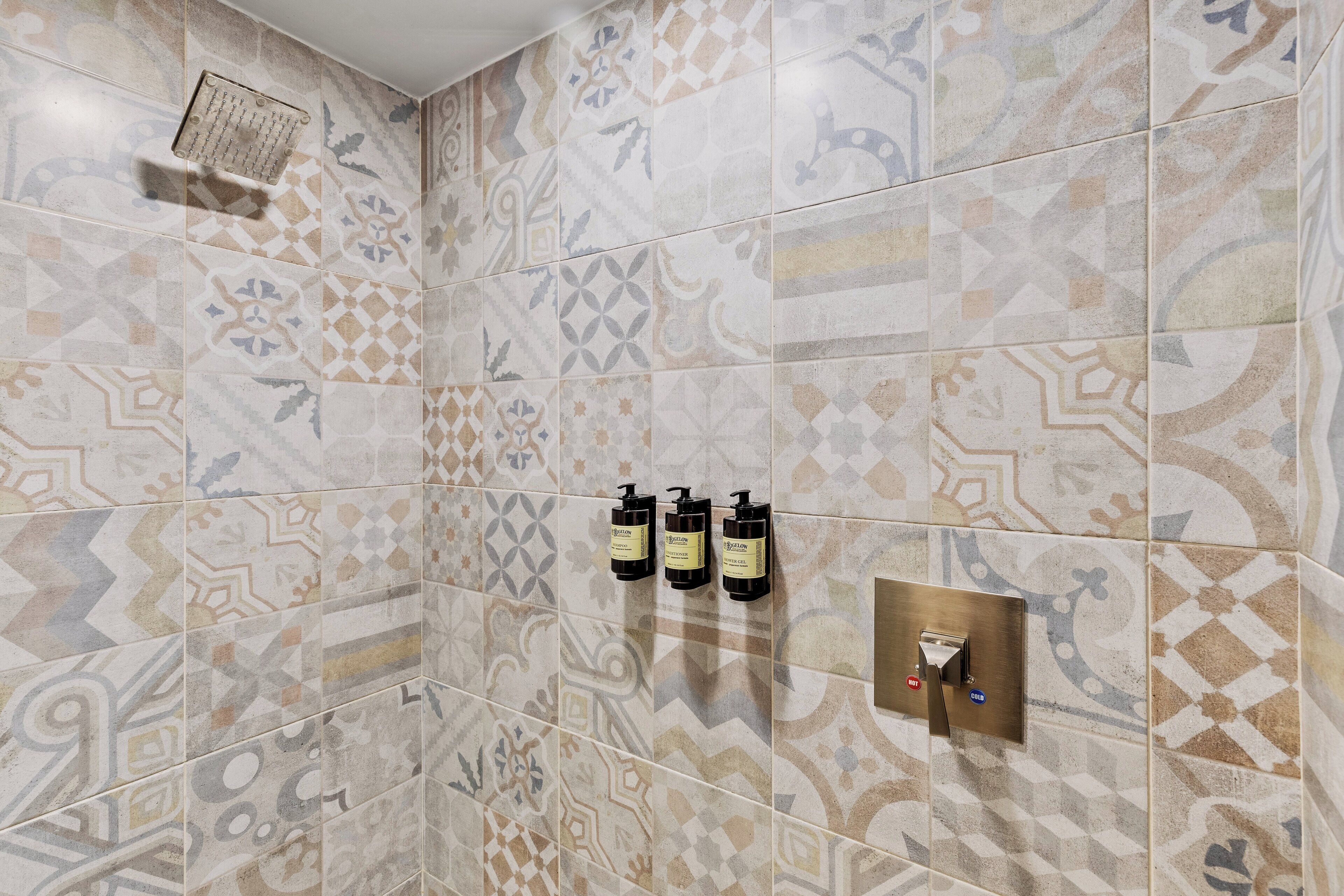 Casa de banho com azulejos estampados, três dispensadores de produtos de higiene e um painel de comando do chuveiro.