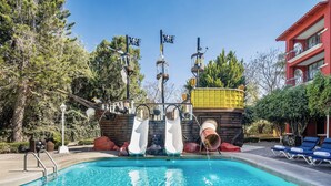 Une piscine avec des toboggans, un bâtiment rouge et des chaises longues.