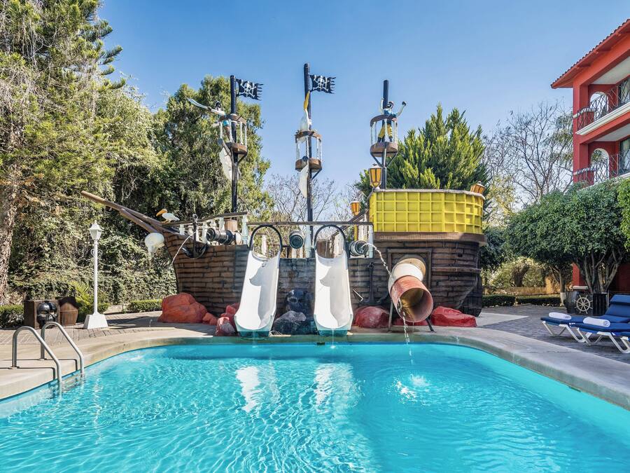 A swimming pool with slides, a red building, and lounge chairs.