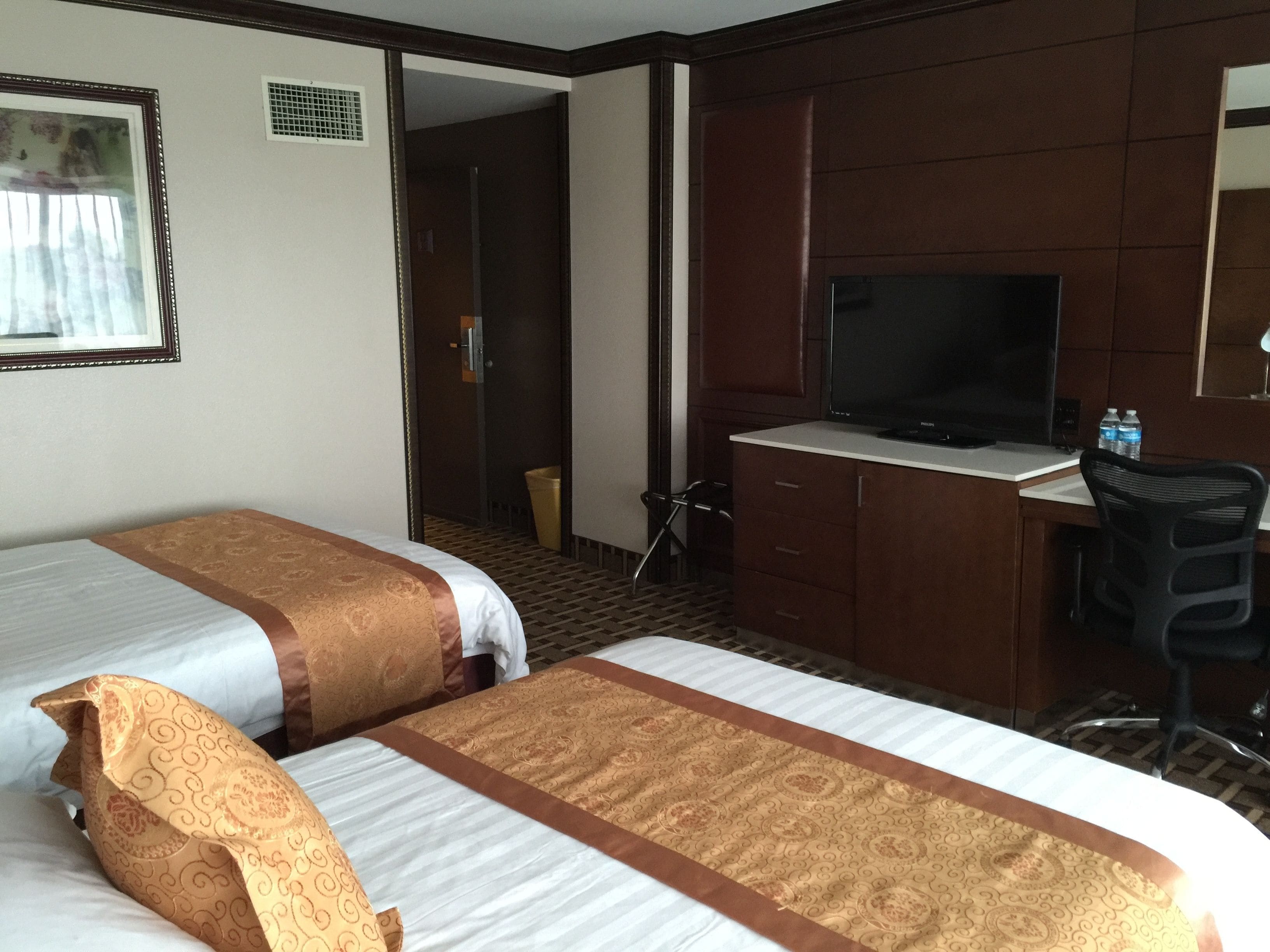 Habitación de hotel con dos camas, un escritorio con televisor y una silla.