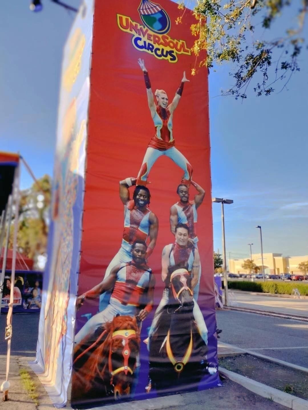 Et stort banner med teksten "UNIVERSAL CIRCUS" og en gruppe optrædende i farverige kostumer.