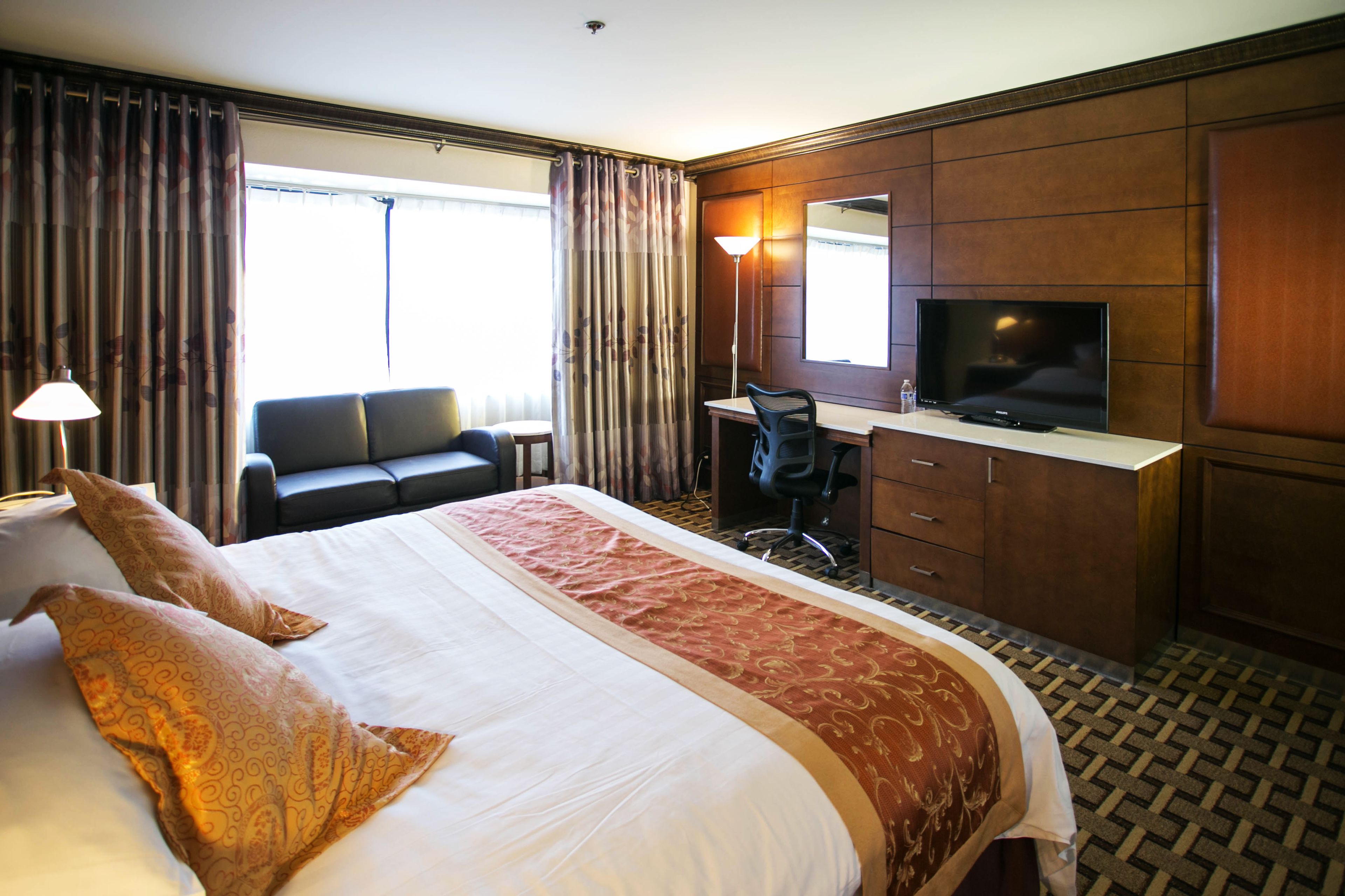 A hotel room with a large bed, a desk with a chair, a television, and a wardrobe.
