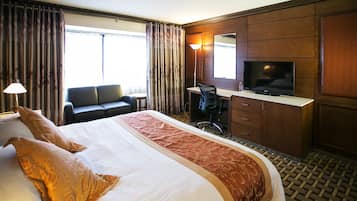 A hotel room with a large bed, a desk with a chair, a television, and a wardrobe.