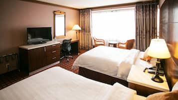 A hotel room with two beds, a desk with a television, a chair, a lamp, and a window with curtains.