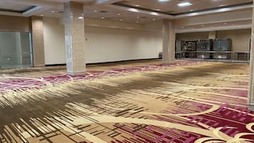 Um amplo hall de hotel com carpete estampado, pilares grandes e divisória de vidro.