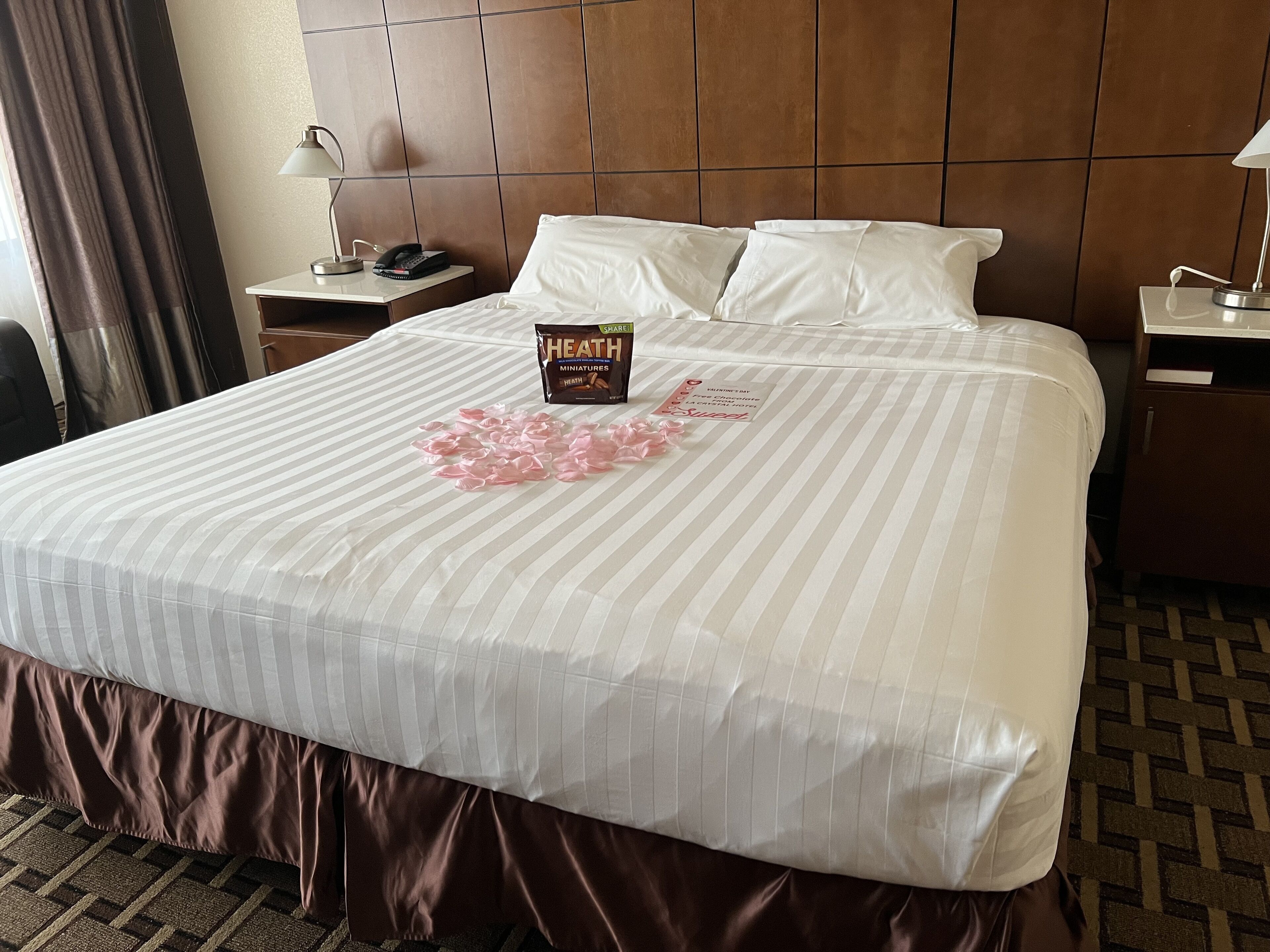 A hotel room with a large bed, a bedside table with a lamp, and a nightstand with a phone.