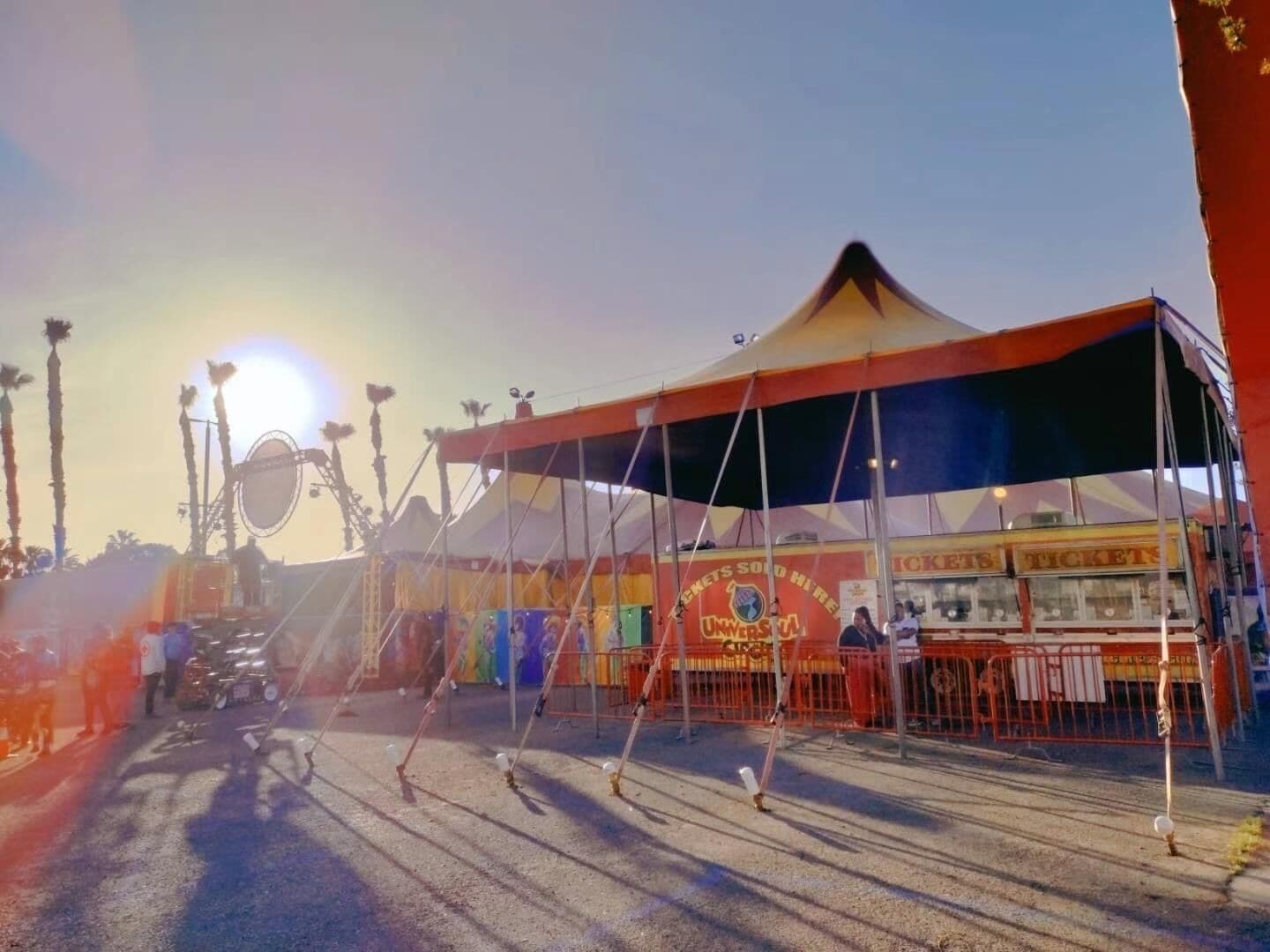 Uma tenda de circo com uma bilheteria e uma roda gigante ao fundo.