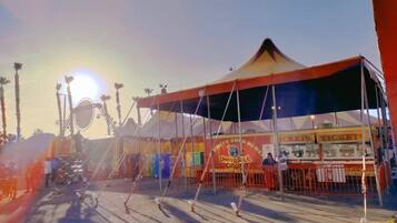 Uma tenda de circo com uma bilheteria e uma roda gigante ao fundo.
