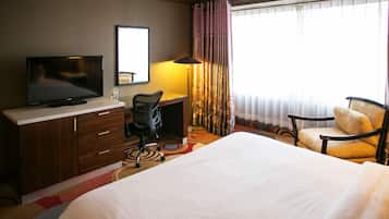 A hotel room with a bed, a desk with a television, a chair, and a window with curtains.