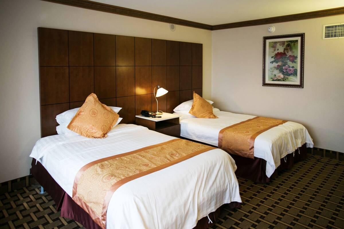 A hotel room with two beds, a nightstand, a lamp, and a framed floral artwork on the wall.