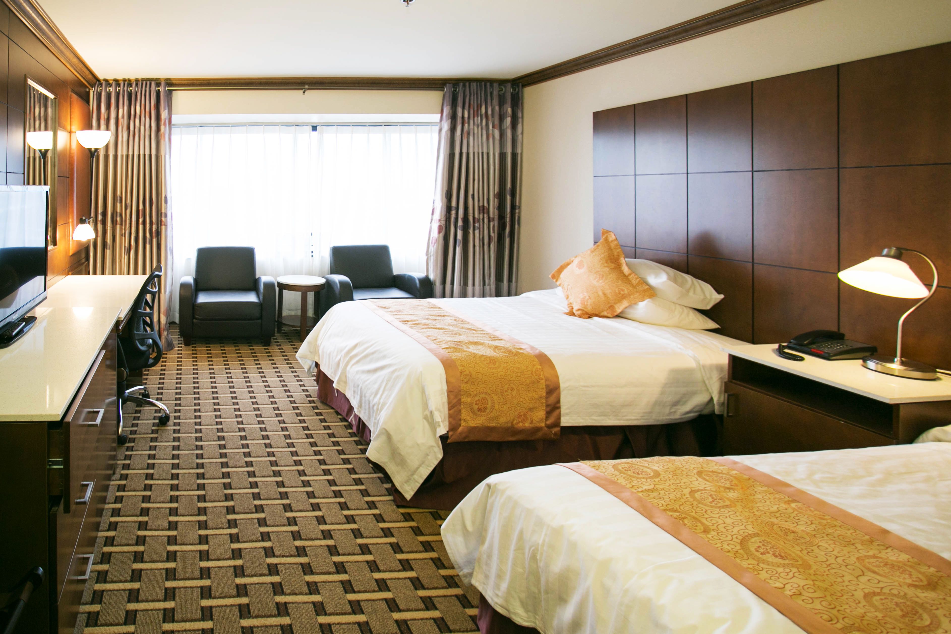 A hotel room with two beds, a desk, a chair, and a small table.