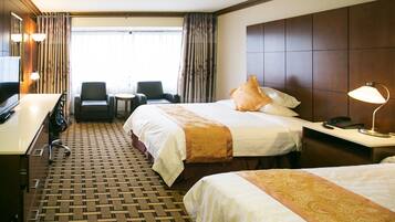 A hotel room with two beds, a desk, a chair, and a small table.