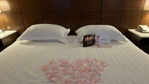 A hotel room with a neatly made bed, a heart-shaped arrangement of rose petals, a minibar, and a sign offering free chocolate. - LA Crystal Hotel - Los Angeles Area (Compton)