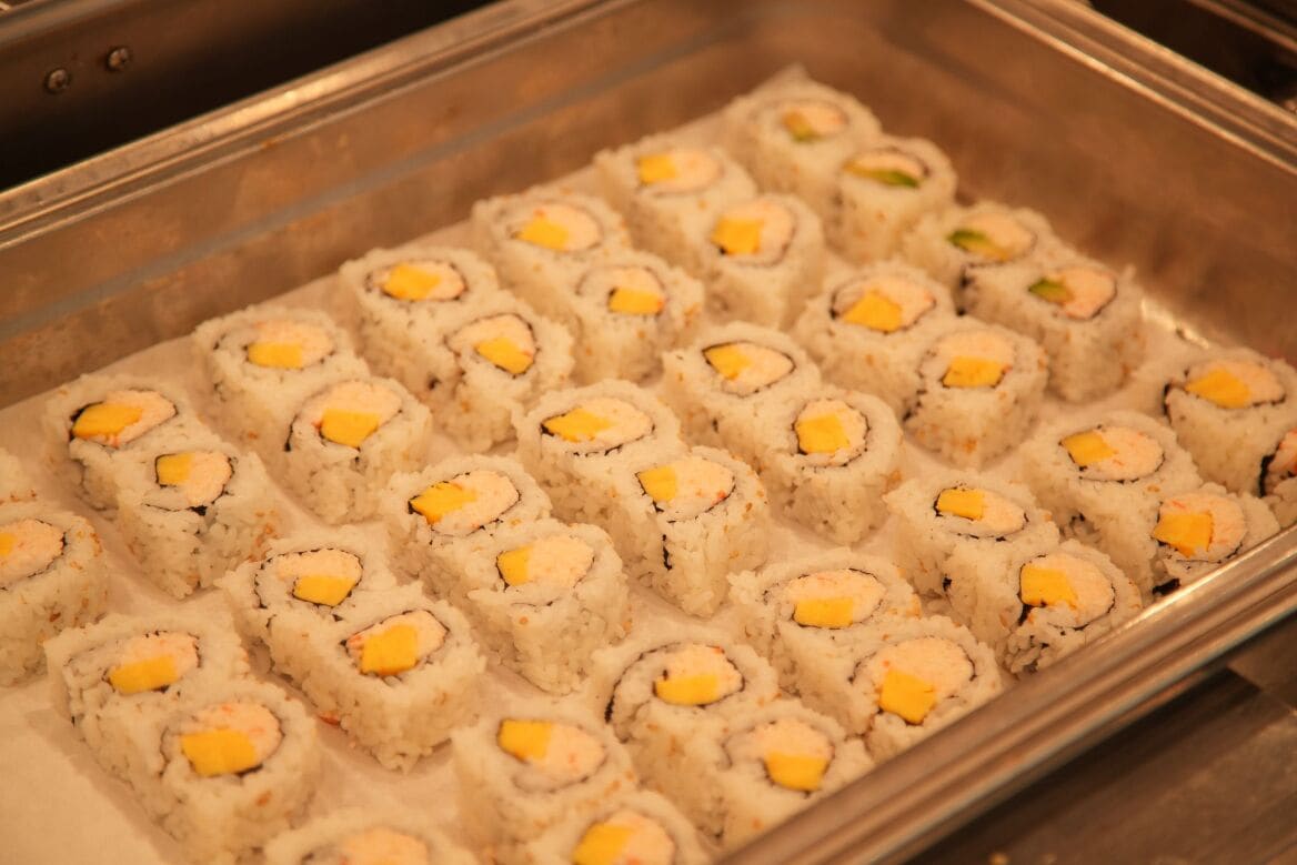 A tray of sushi rolls with yellow toppings.