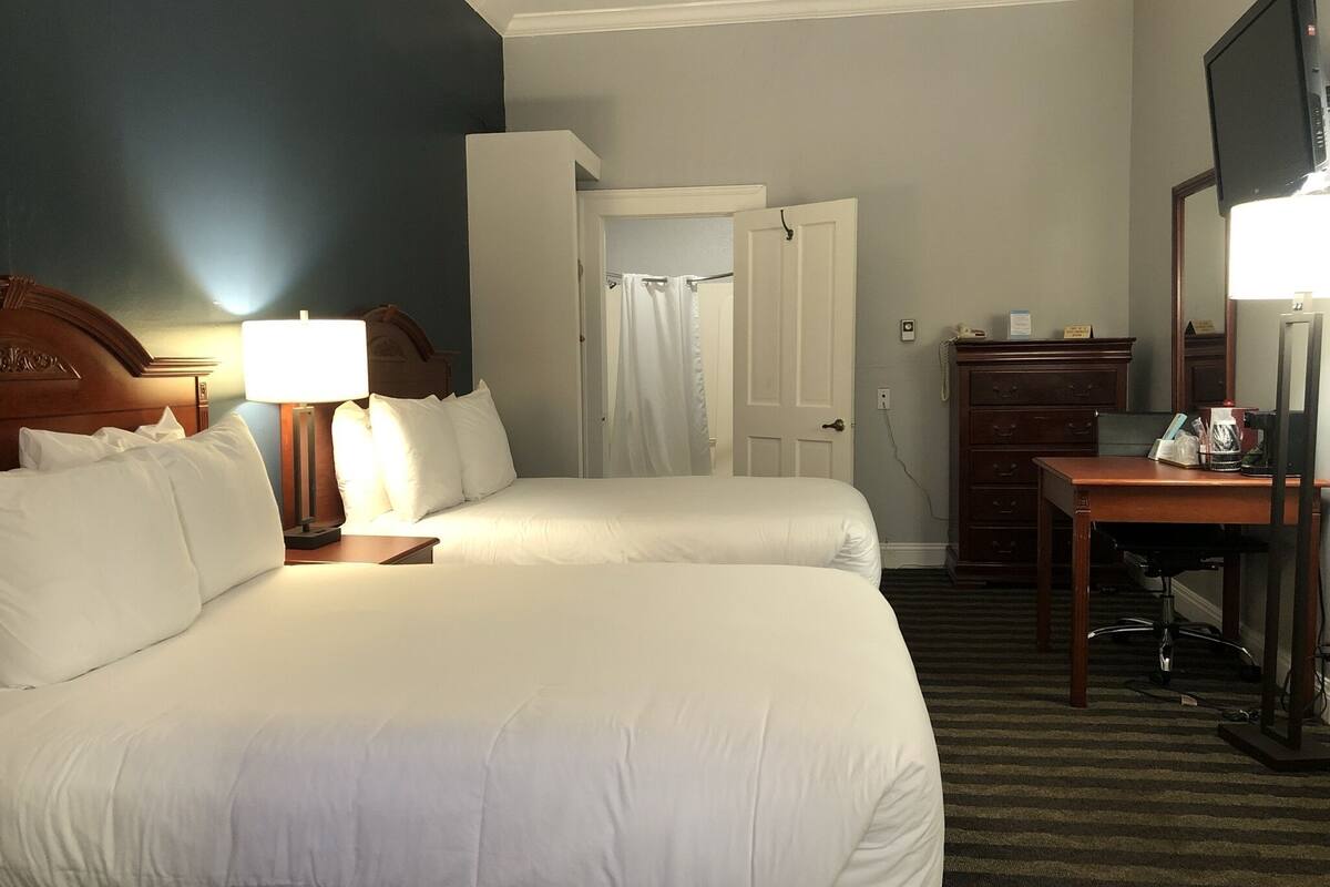 Quarto de hotel com duas camas, uma escrivaninha, uma cômoda e uma televisão.