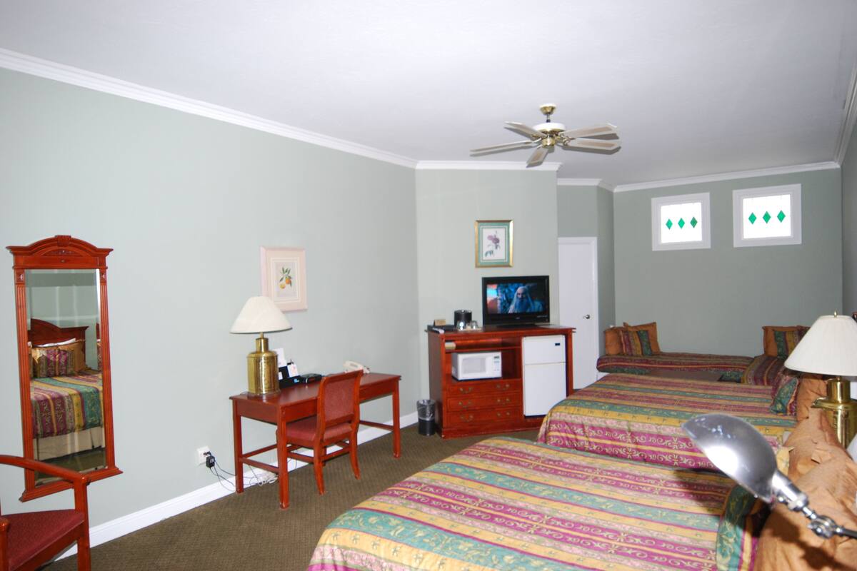 Quarto de hotel com duas camas, uma escrivaninha, televisão, espelho e ventoinha no teto.