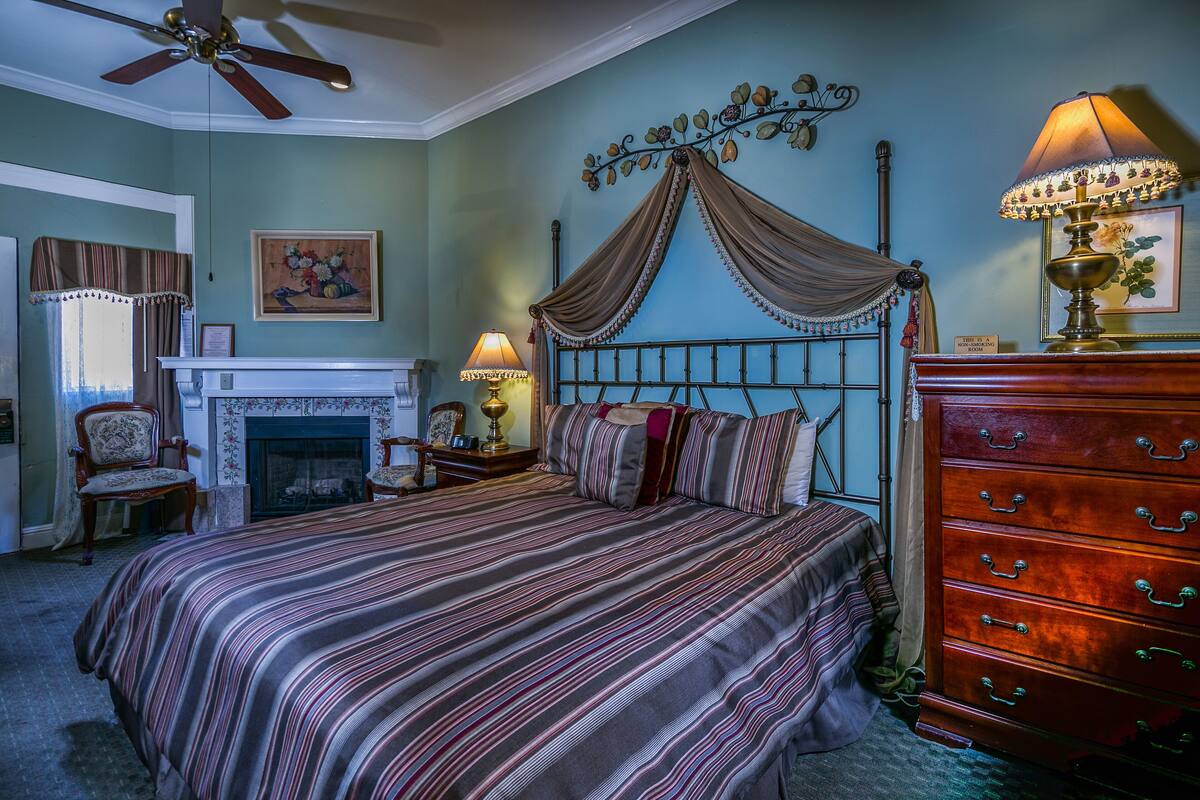 Um quarto com cama de dossel, lareira, cómoda de madeira e ventoinha no teto.