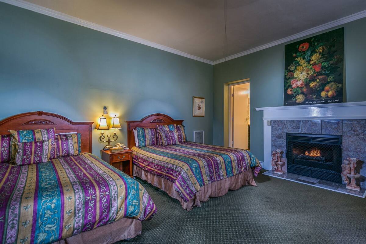 Quarto de hotel com duas camas, lareira e pintura floral na parede.