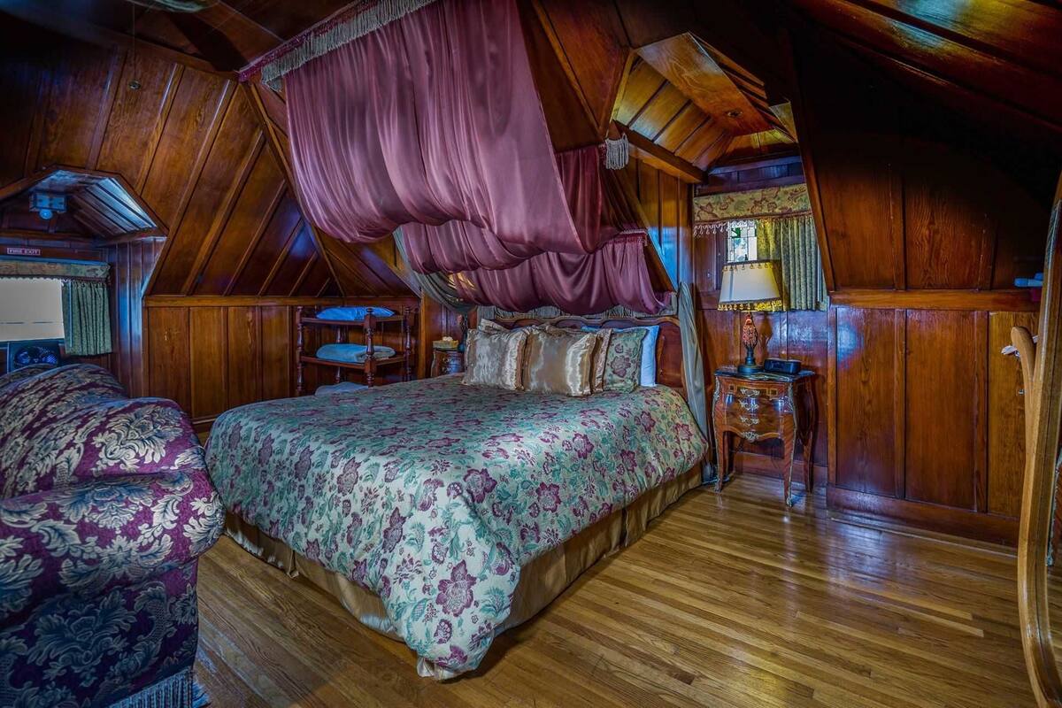 Quarto com cama de dossel, piso de madeira e mesa de cabeceira com abajur.