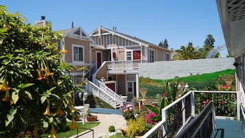 Uma casa de dois andares com uma varanda, escadaria e jardim com diversas plantas e flores.