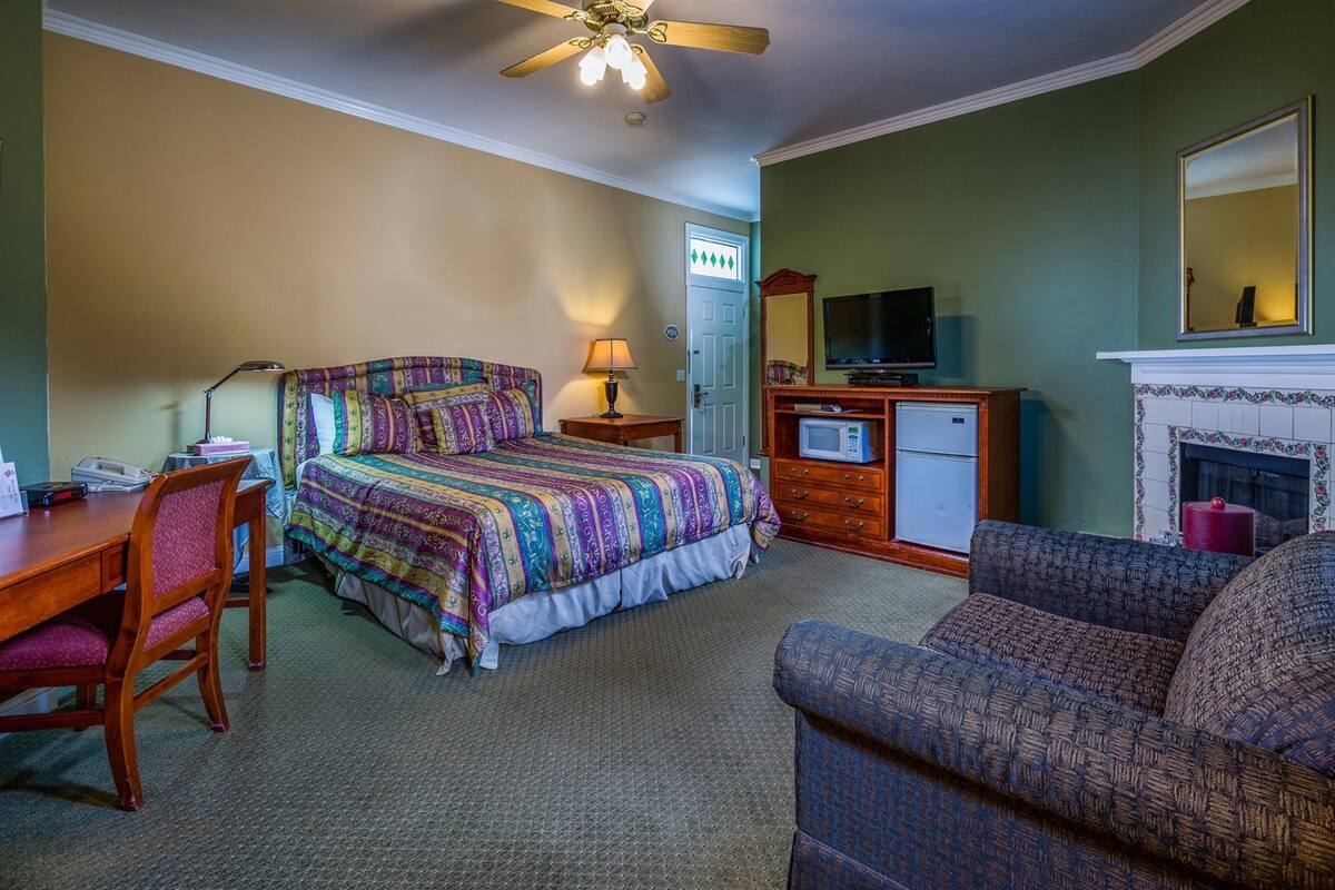 Quarto de hotel com cama, escrivaninha, cadeira, televisão, micro-ondas e lareira.