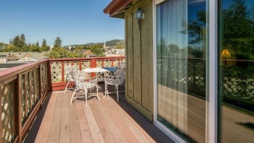 Um deck de madeira com mesa e cadeiras, uma porta de vidro e vista para uma área residencial.