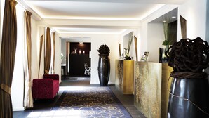 A hotel lobby with a dark blue carpet, a red chair, and a large vase with a decorative top. - Schloss Huenigen (Konolfingen)