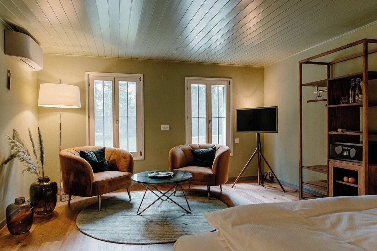 Una habitación acogedora con dos sillones de cuero, una mesita redonda, una estantería y un televisor sobre un trípode.