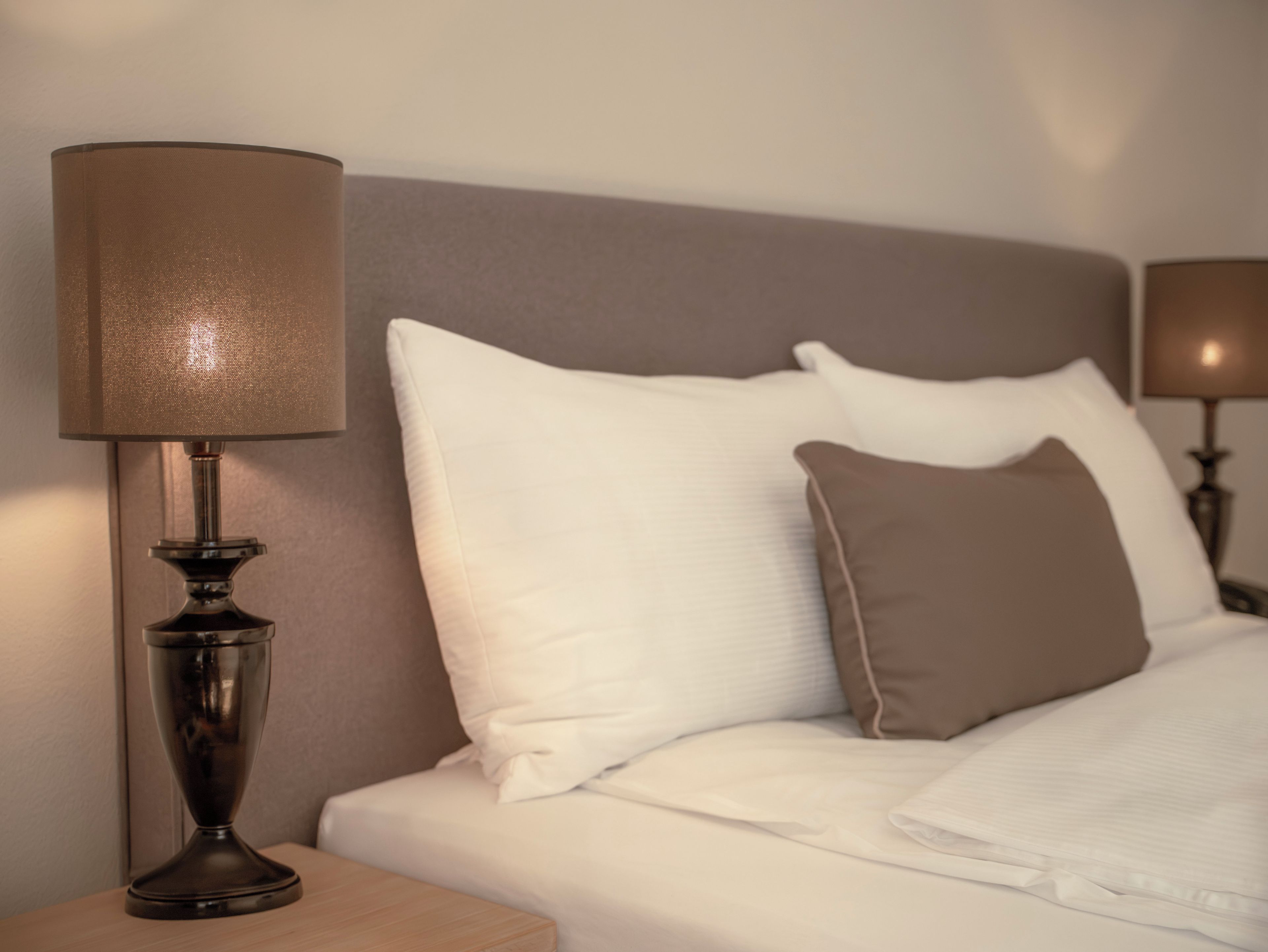 A neatly made bed with white and brown pillows, a bedside lamp, and a wooden nightstand.