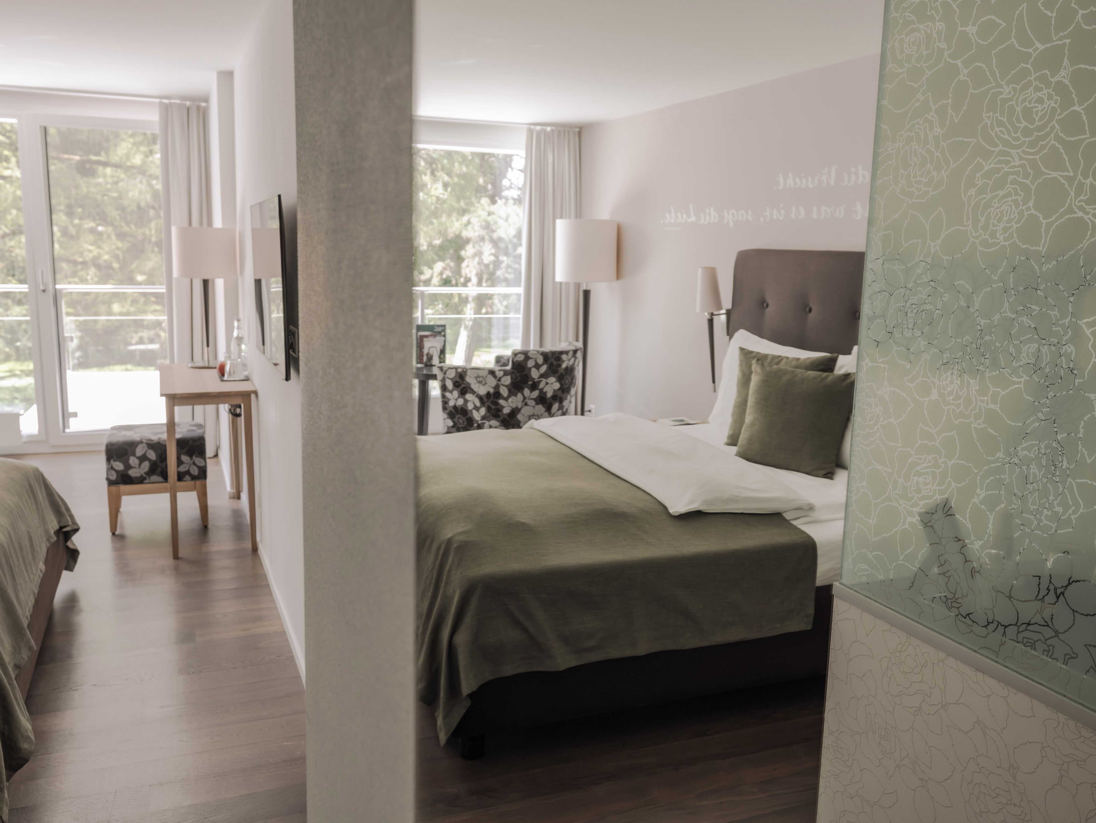 Un dormitorio moderno con cama, mesita de noche, silla y vistas al exterior a través de amplios ventanales.