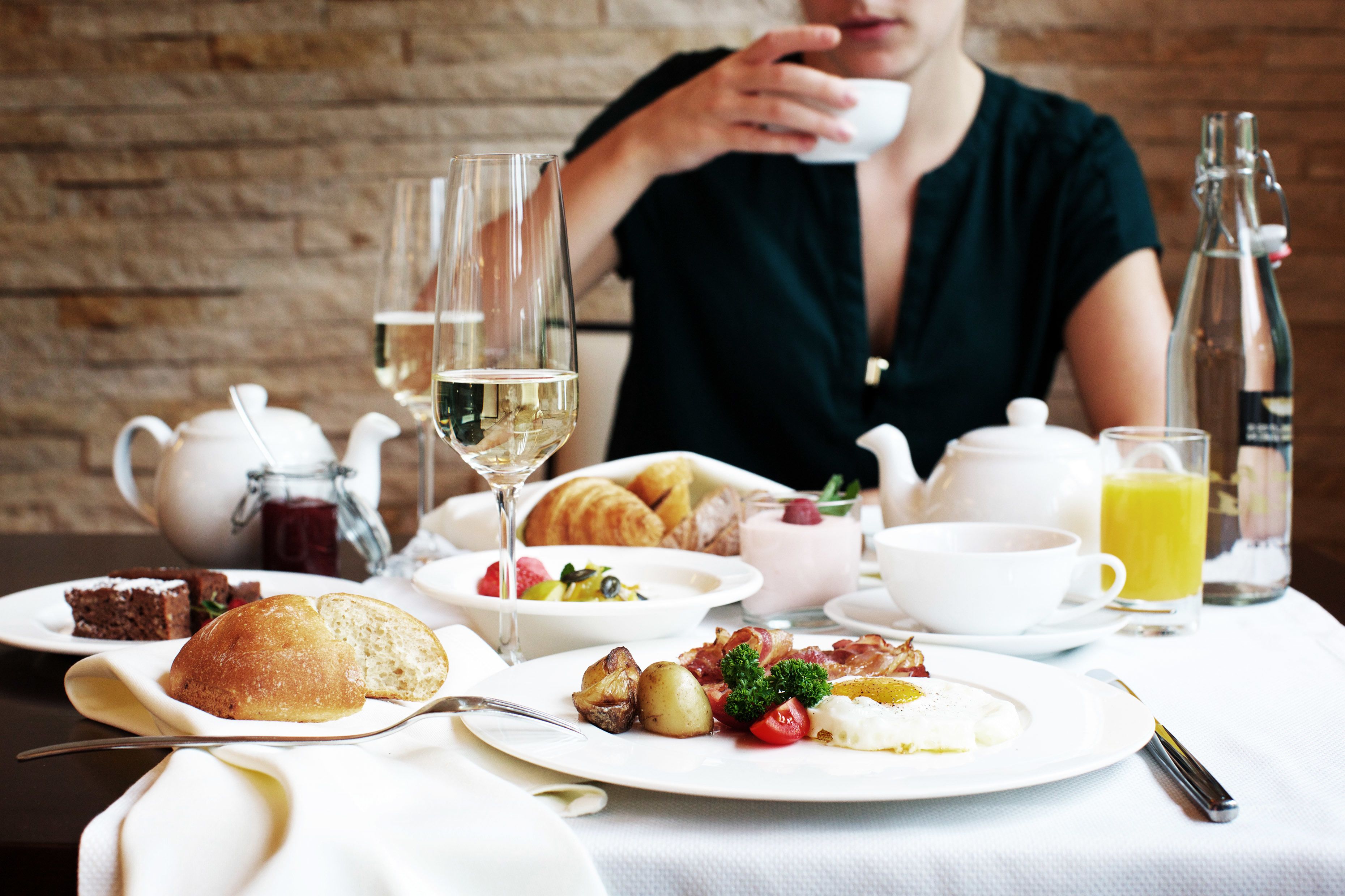 A breakfast setting with a variety of dishes, including croissants, fruit, and eggs, along with beverages like wine and juice.