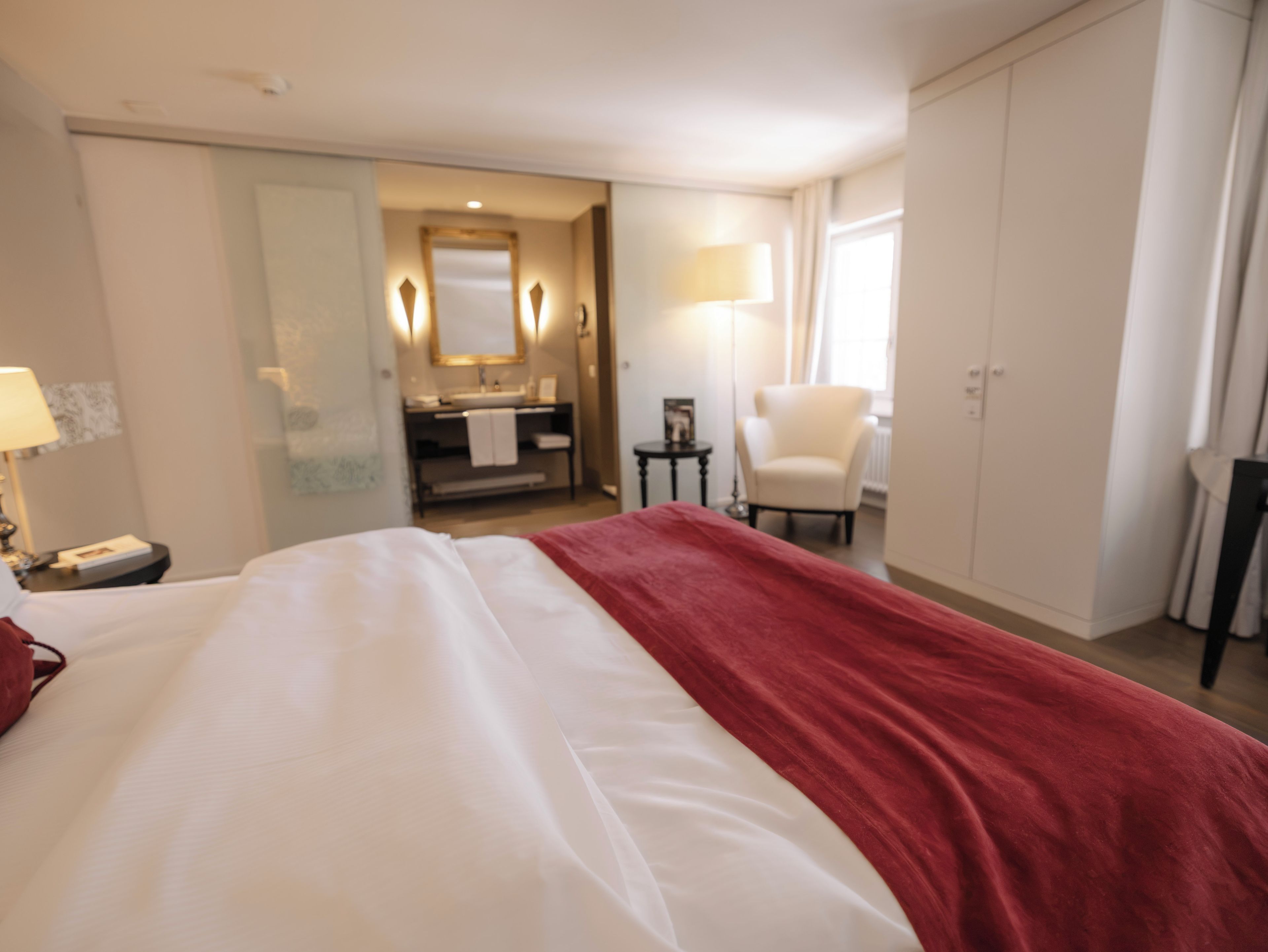 A hotel room with a bed, a desk, a chair, a wardrobe, and a bathroom visible through an open door.