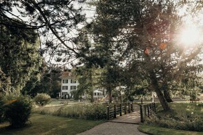 A pathway leading to a white building with a green roof, surrounded by dense trees and a grassy area. - Schloss Huenigen (Konolfingen)