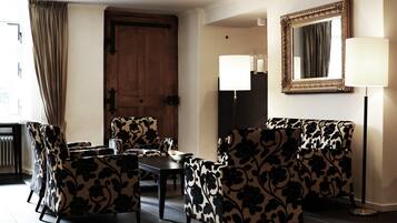 A room with a wooden door, a table with chairs, a floor lamp, and a mirror on the wall.